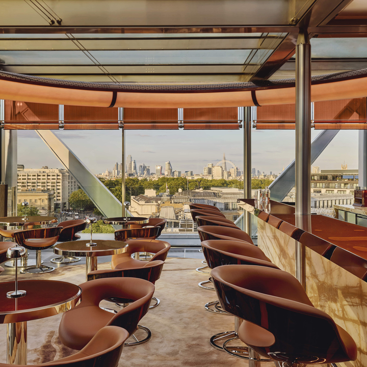 Stylish rooftop bar with sleek seating, a polished marble counter, and panoramic city views framed by floor-to-ceiling windows.