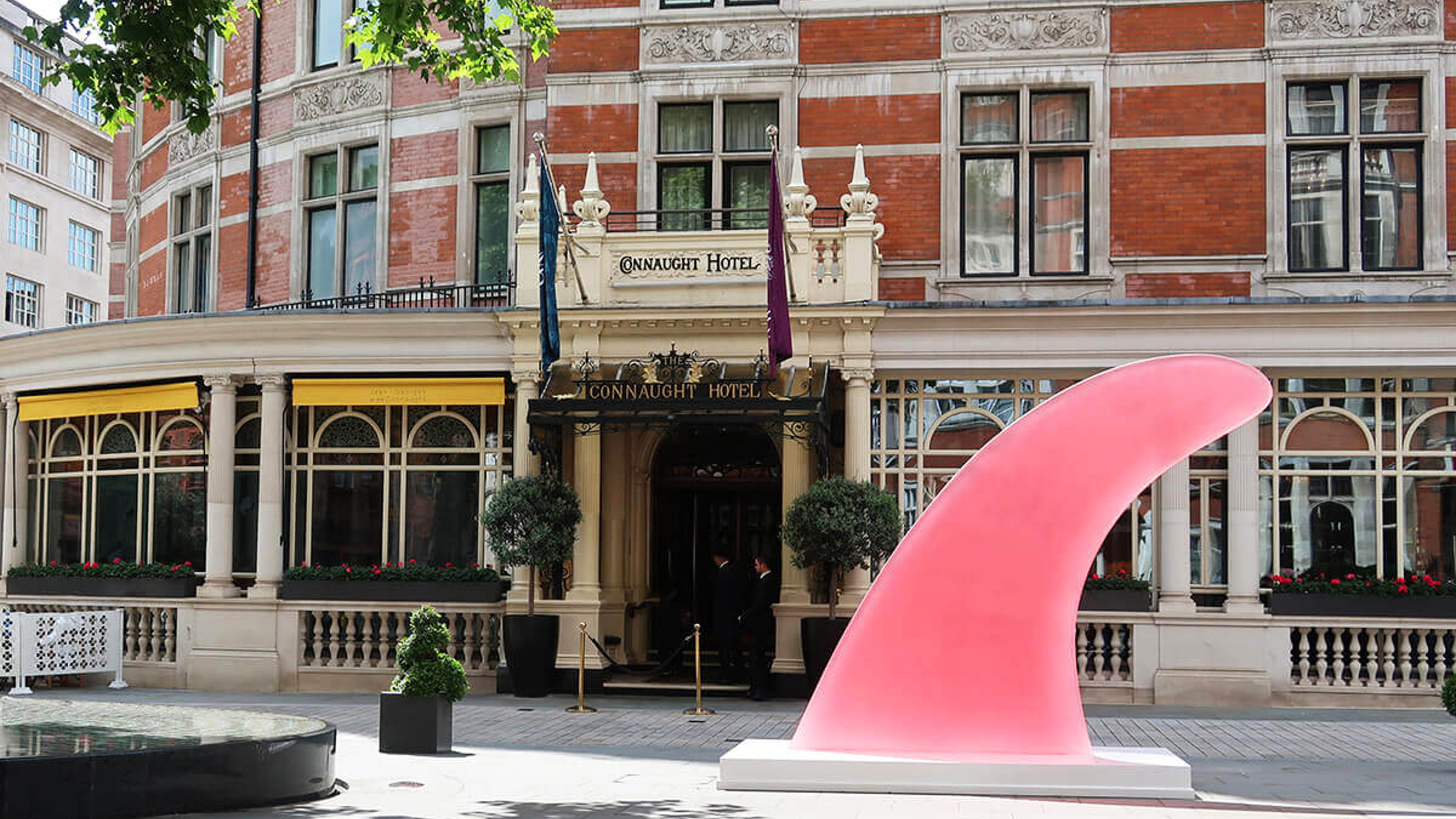Exterior of The Connaught Hotel with a large pink sculptural artwork displayed in front, surrounded by trees and classic architecture.