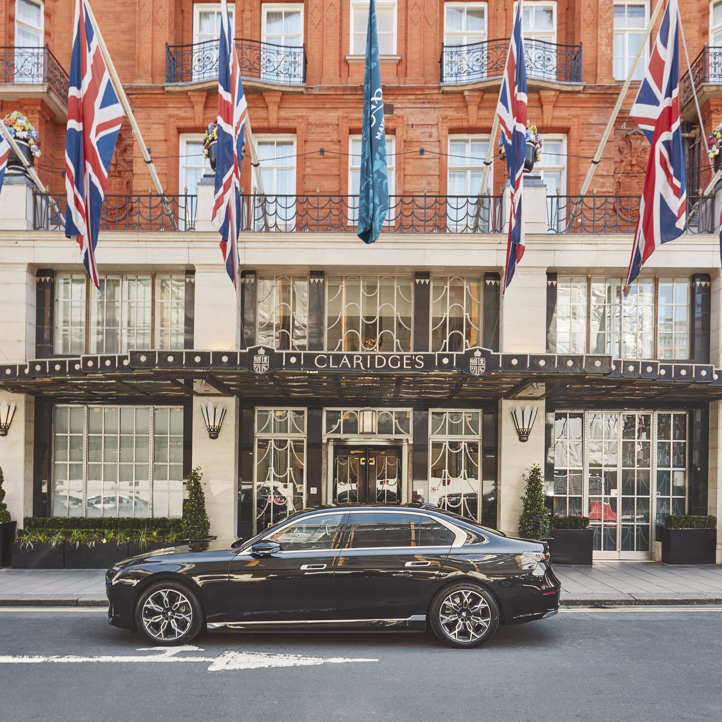 The grand entrance of Claridge's, adorned with Union Jack flags and a sleek black car parked outside.