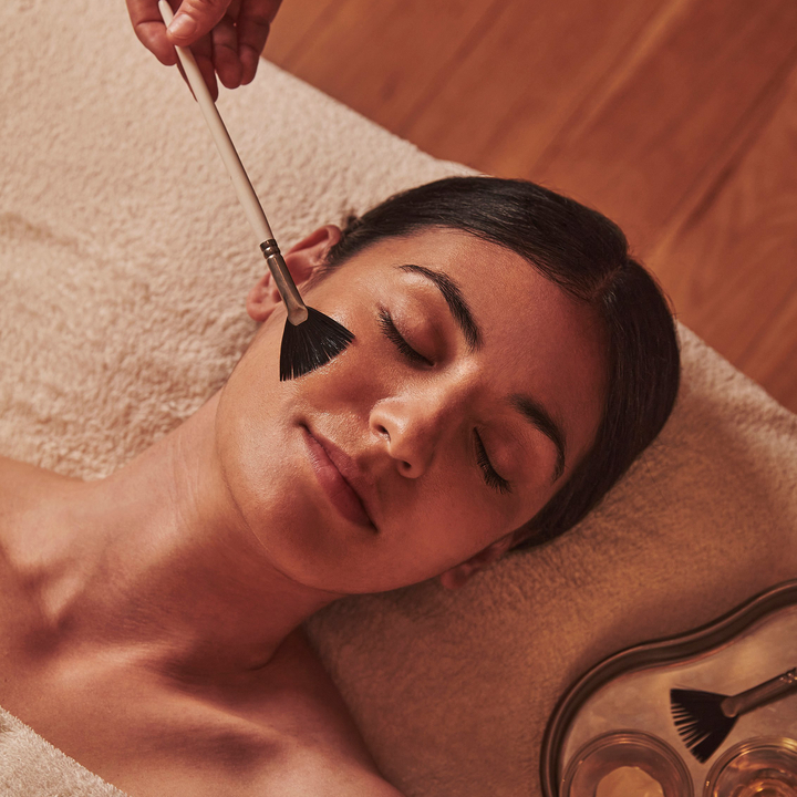 A serene moment of a woman receiving a luxurious facial treatment, as a gentle brush applies a soothing mask.
