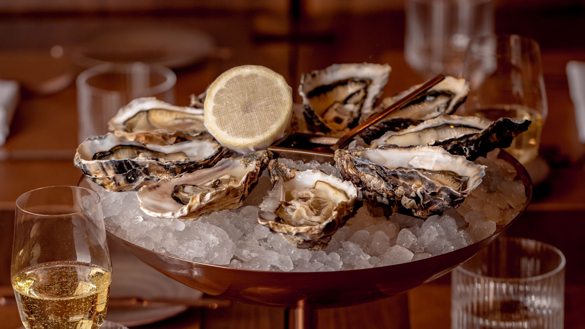 Oysters on ice served with lemon, alongside sparkling wine in a refined dining setting.