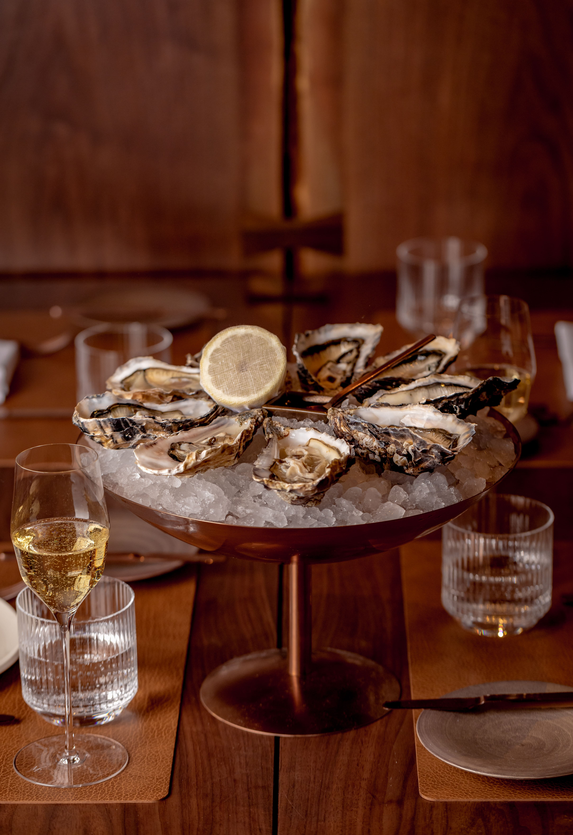 Oysters on ice served with lemon, alongside sparkling wine in a refined dining setting.