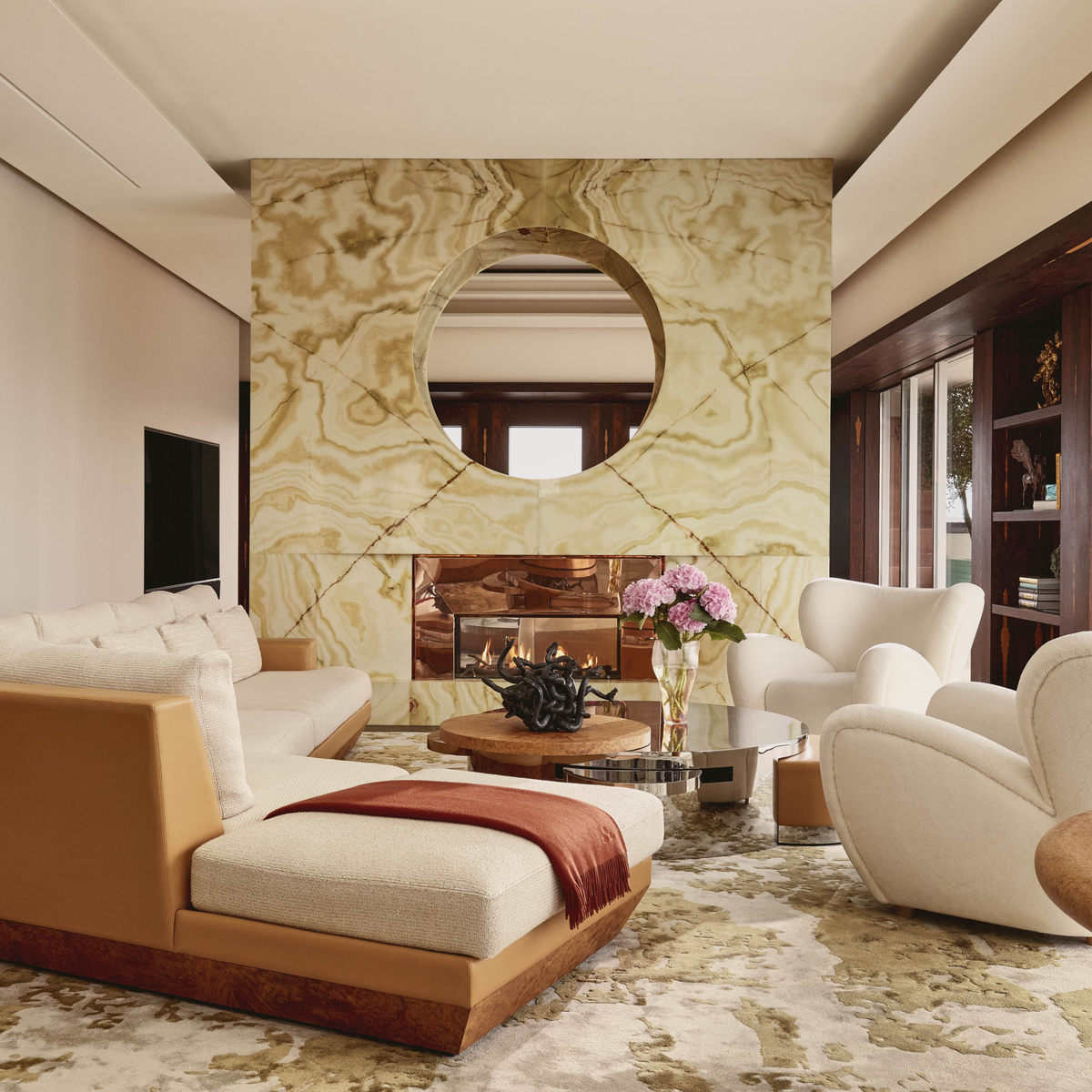 Contemporary living space in Claridge’s Penthouse featuring sculptural armchairs, a circular marble fireplace, abstract art, and soft neutral-toned furnishings.