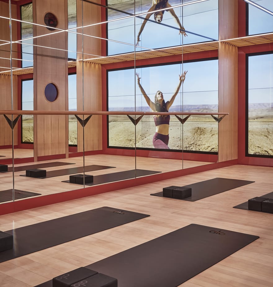 Surrenne Yoga Studio which has mirrored walls, wooden floors, yoga mats, and blocks, featuring large scenic desert imagery on screens.