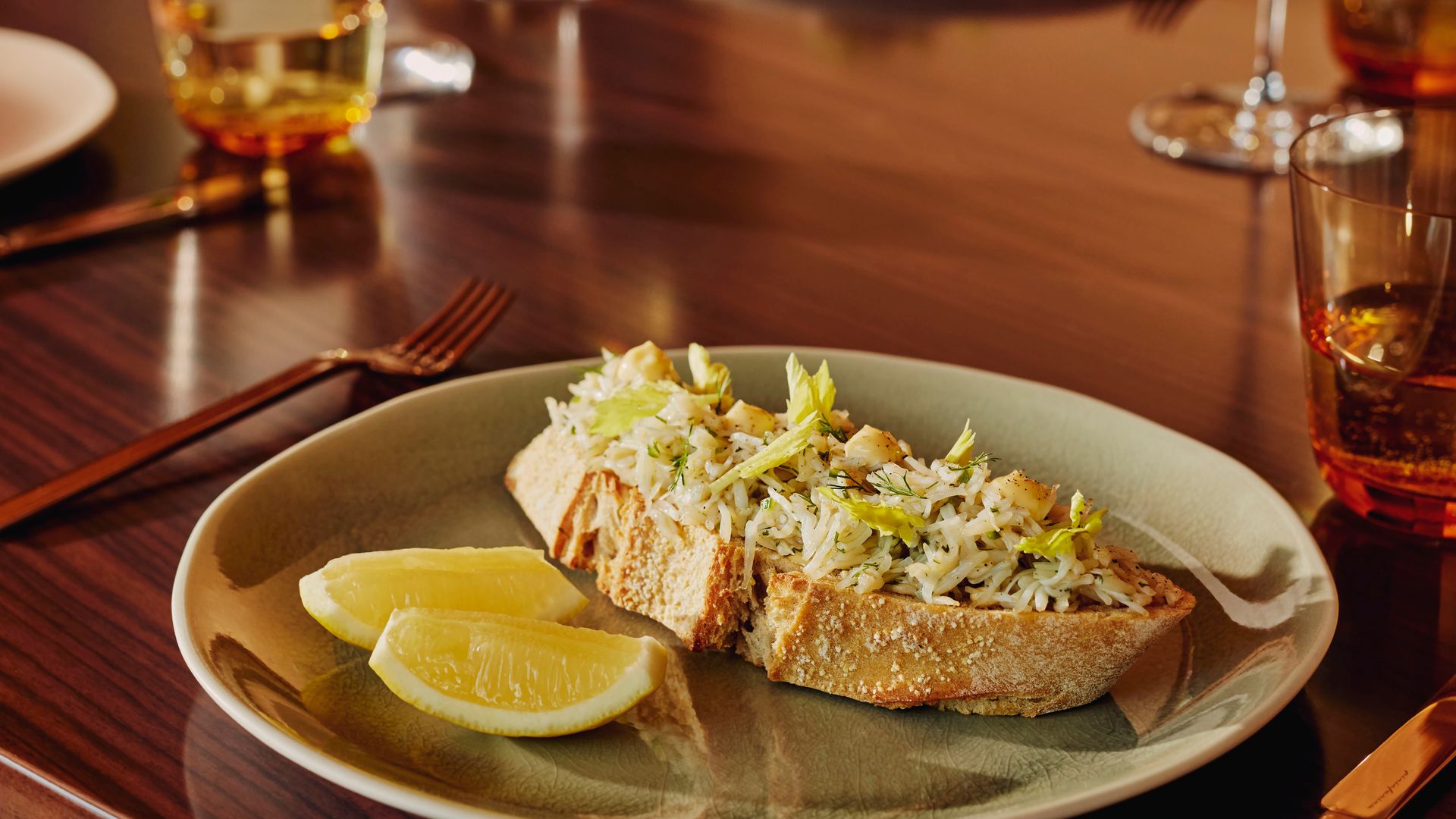 Toasted crab salad on sourdough, served with lemon wedges and wine in a restaurant setting.