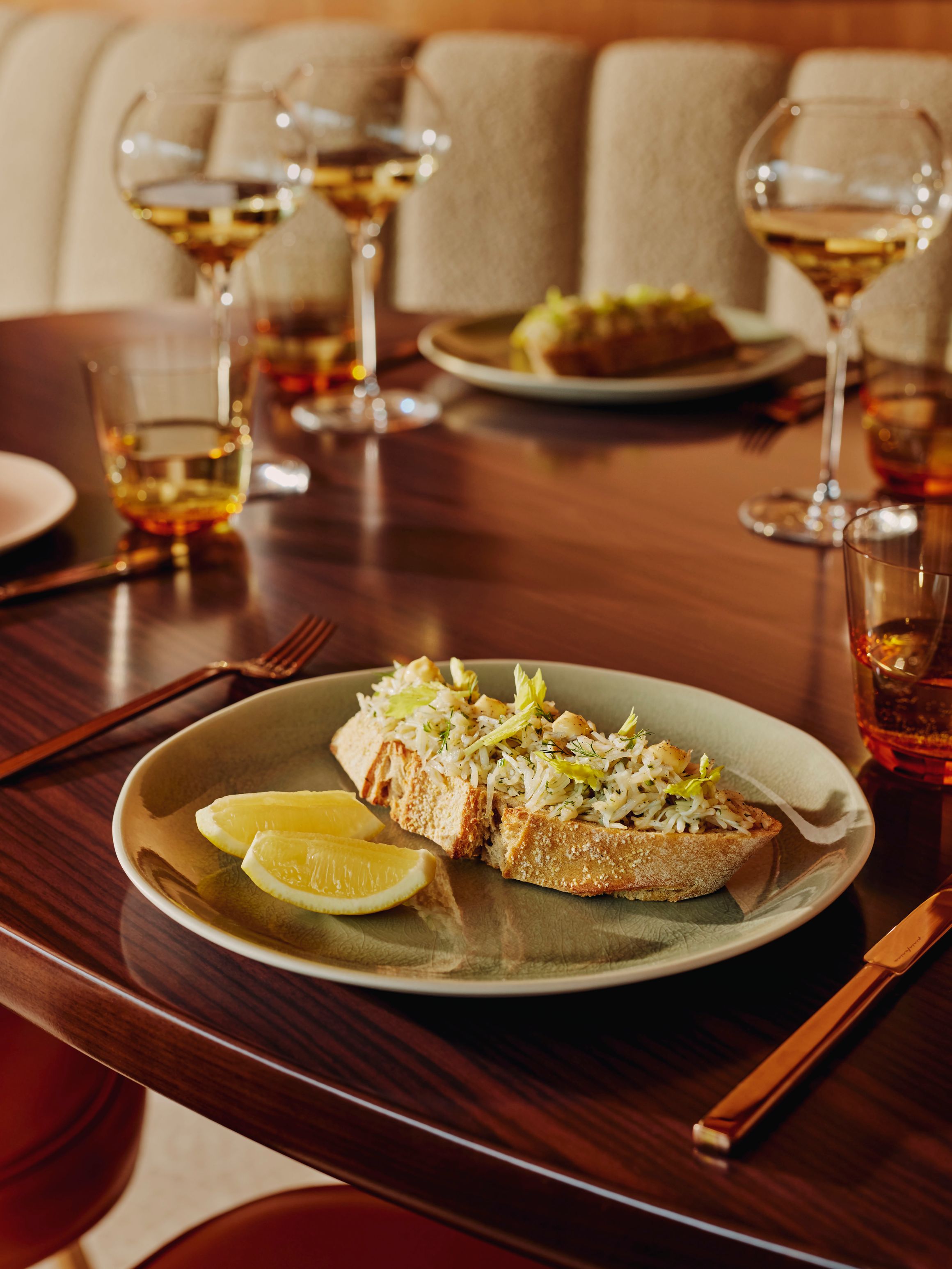 Toasted crab salad on sourdough, served with lemon wedges and wine in a restaurant setting.