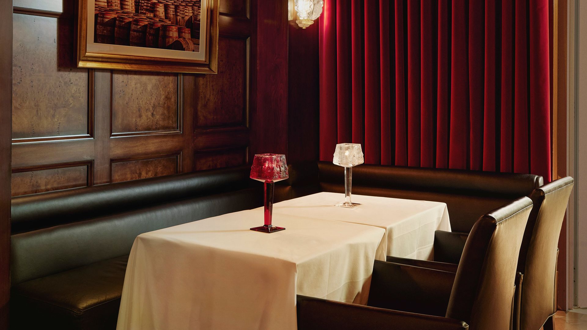 Intimate whisky bar with dark wood paneling, red velvet drapes, and candle-lit table for two.
