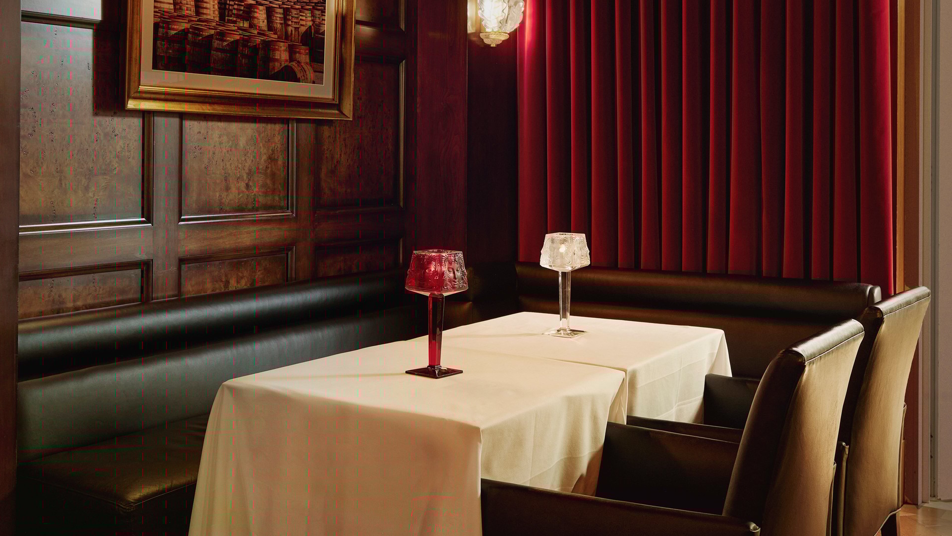Intimate whisky bar with dark wood paneling, red velvet drapes, and candle-lit table for two.