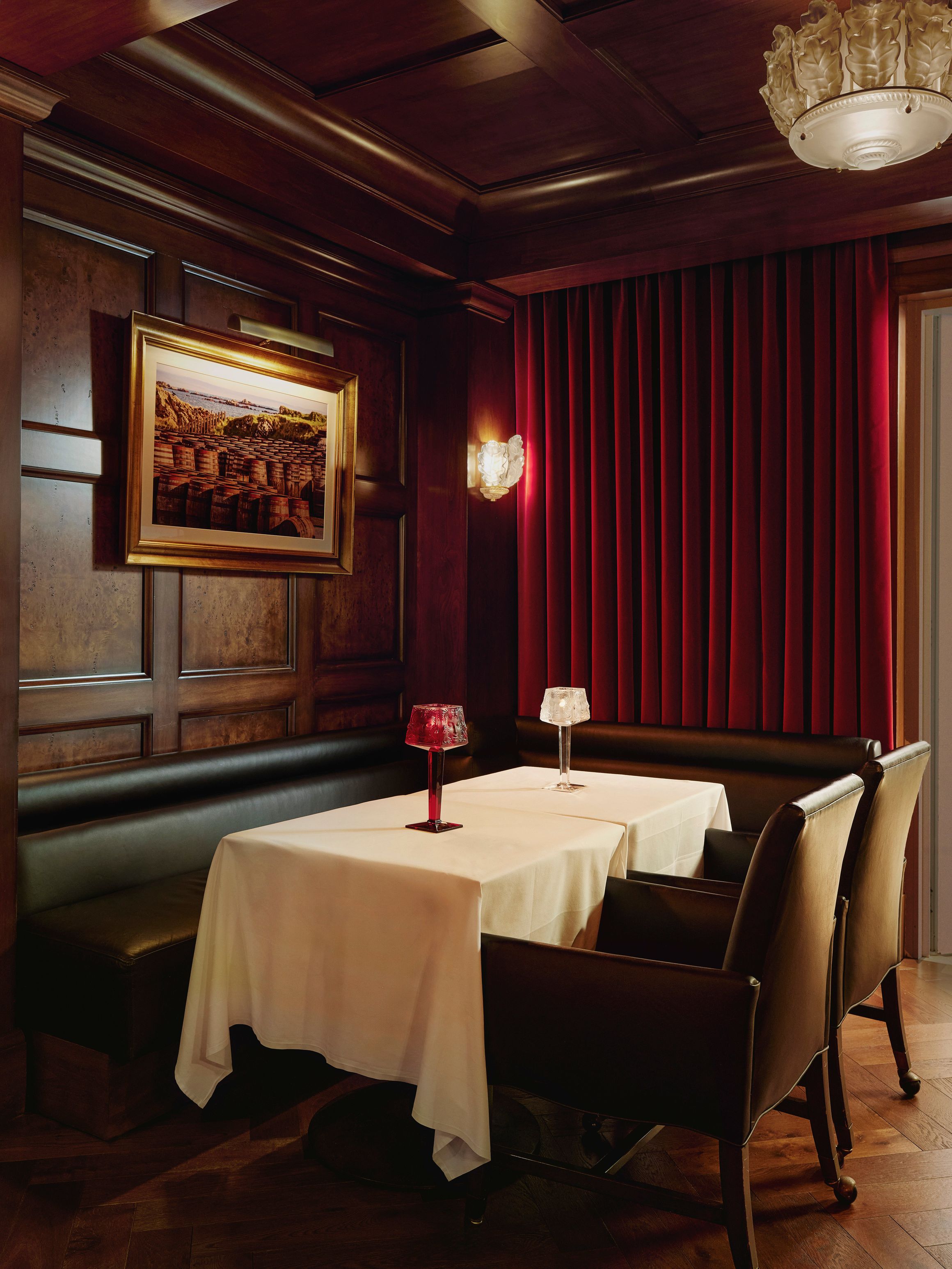 Intimate whisky bar with dark wood paneling, red velvet drapes, and candle-lit table for two.