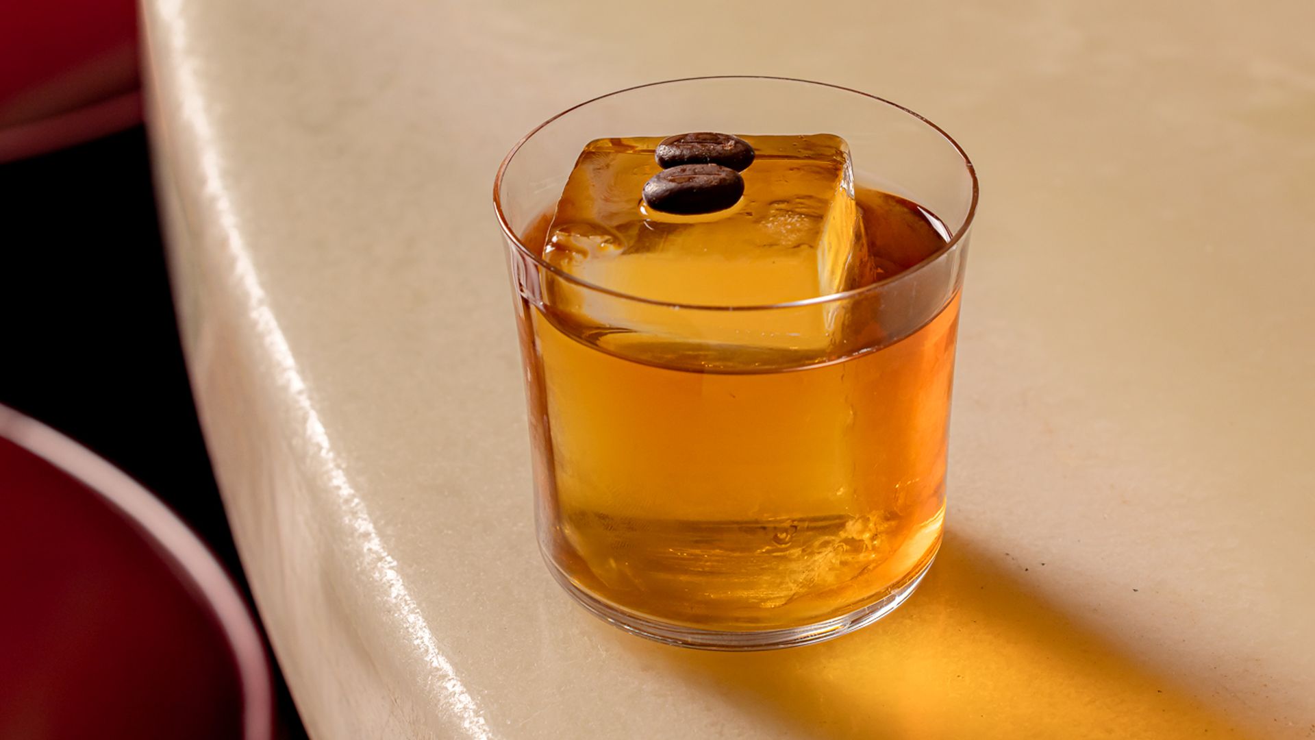 Classic whiskey cocktail with a large ice cube, resting on a sleek marble bar.