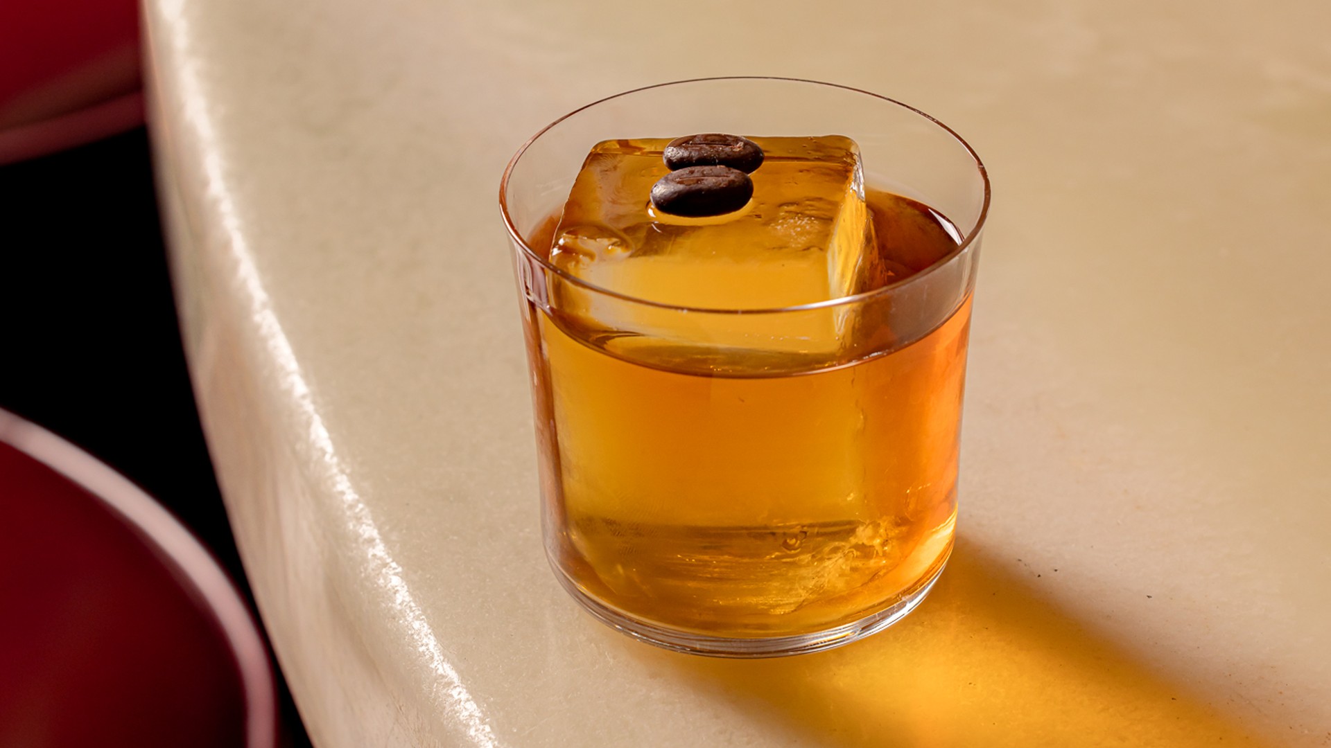 Classic whiskey cocktail with a large ice cube, resting on a sleek marble bar.