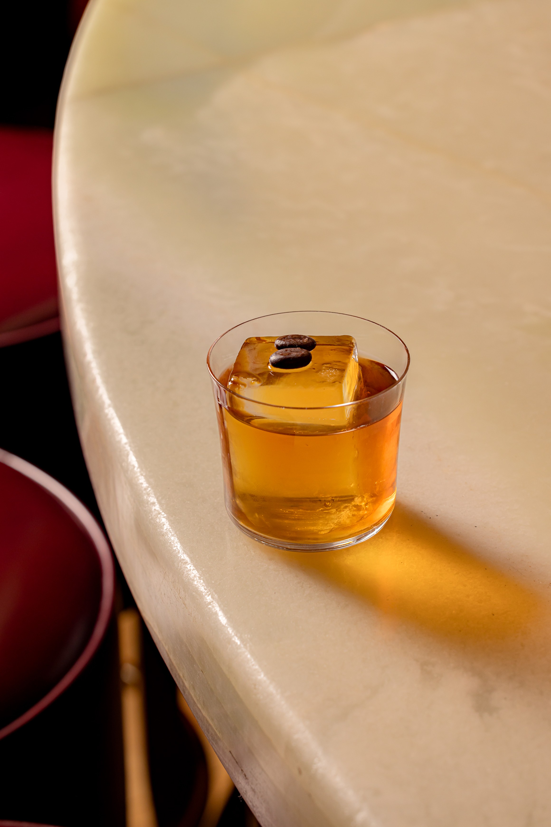 Classic whiskey cocktail with a large ice cube, resting on a sleek marble bar.
