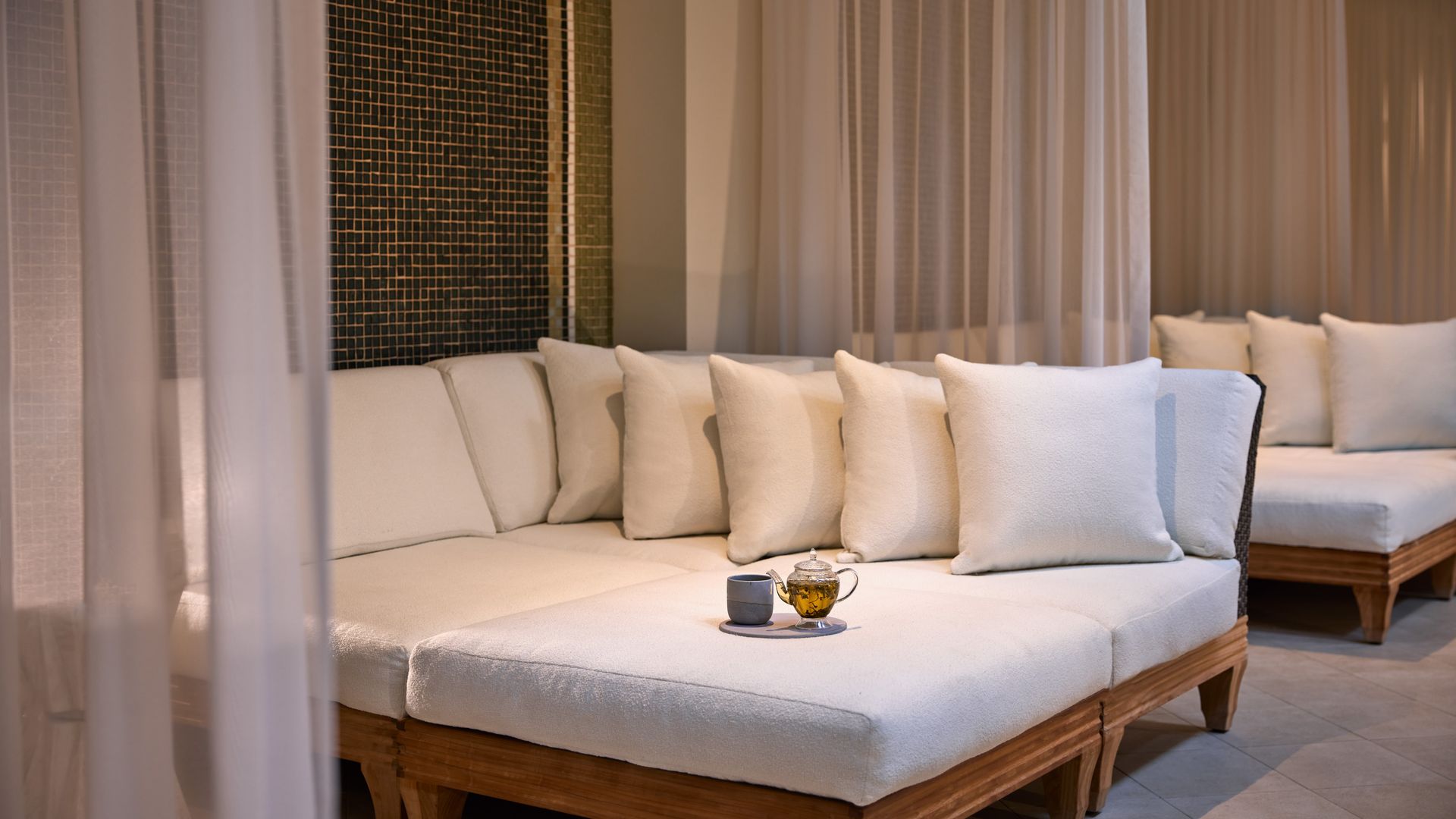 A serene seating area with white cushioned loungers, soft curtains, and a tranquil atmosphere, perfect for relaxation.