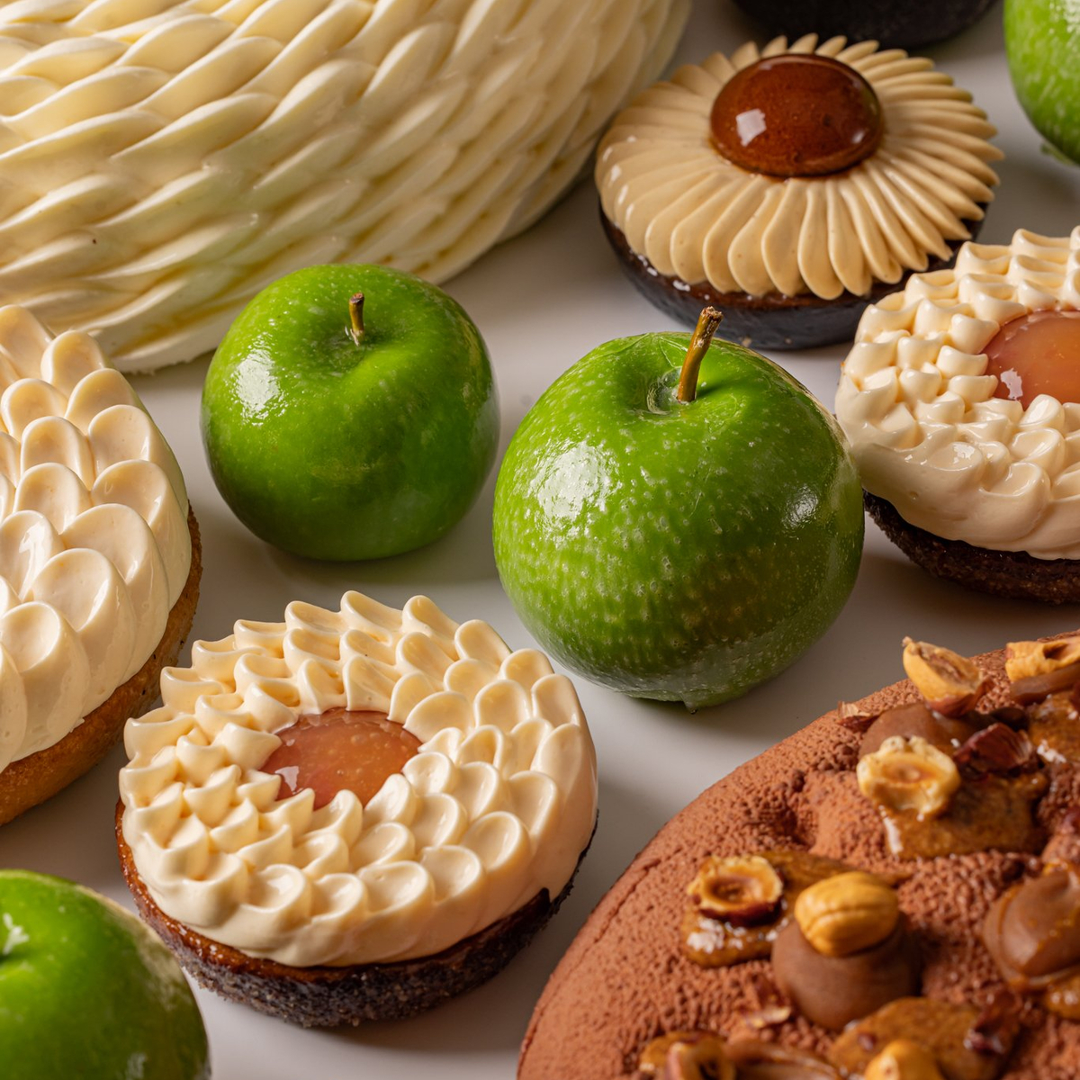 A delectable assortment of gourmet desserts featuring intricate pastries, chocolate confections, and fresh green apples as accents.