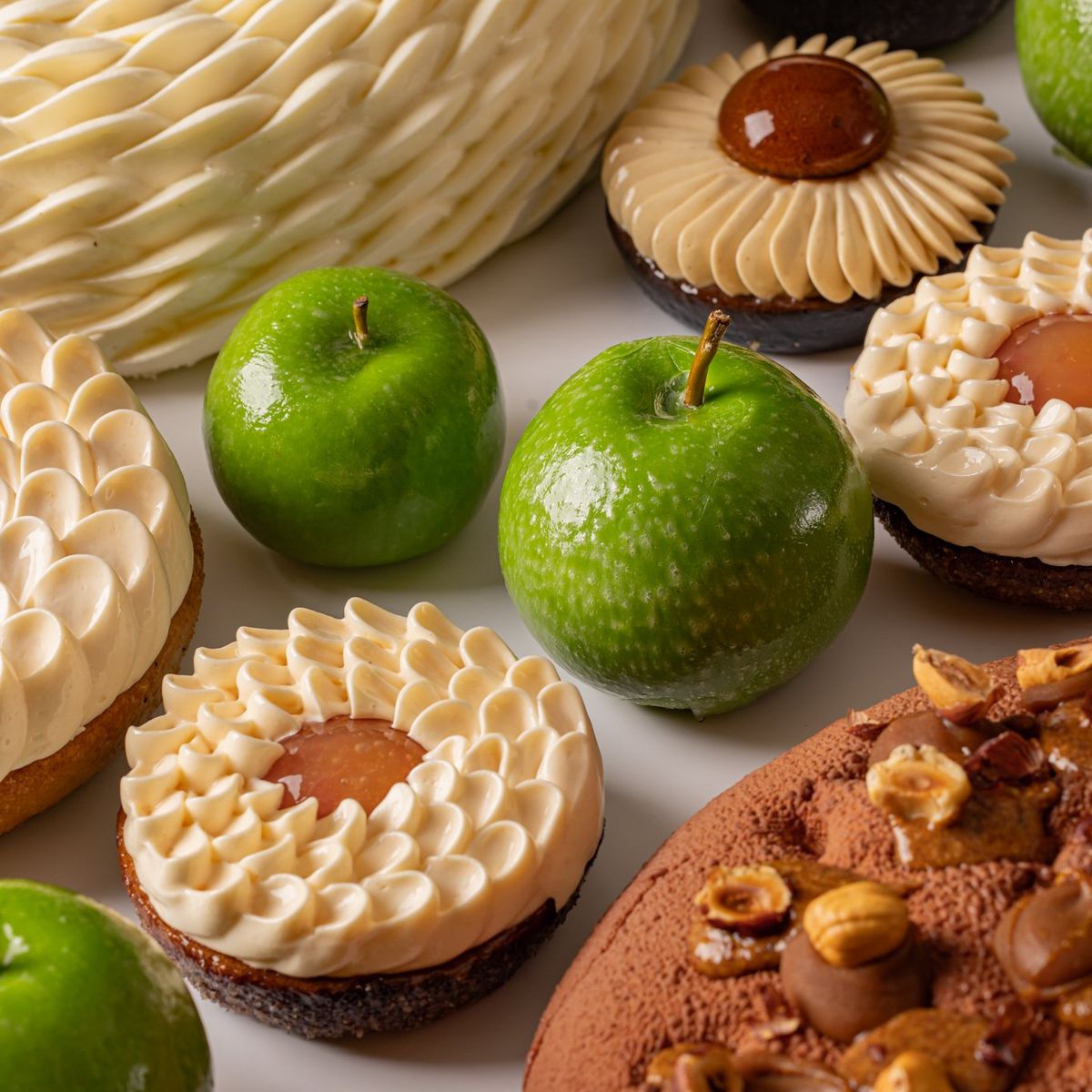 A delectable assortment of gourmet desserts featuring intricate pastries, chocolate confections, and fresh green apples as accents.