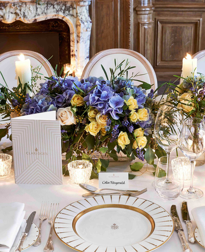 Close-up of a formal table setting with gold-rimmed plates, candles, and purple and yellow floral arrangement at Claridge’s.