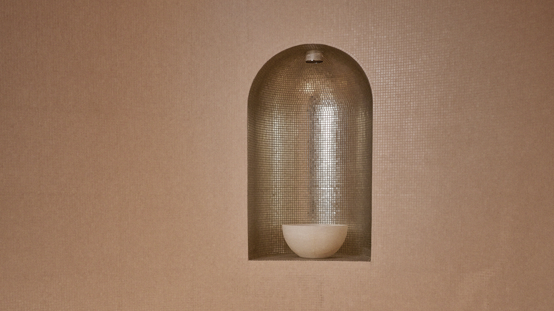 A luxurious steam room with warm-toned walls, a niche featuring a glowing bowl, and a curved seating area designed for comfort.