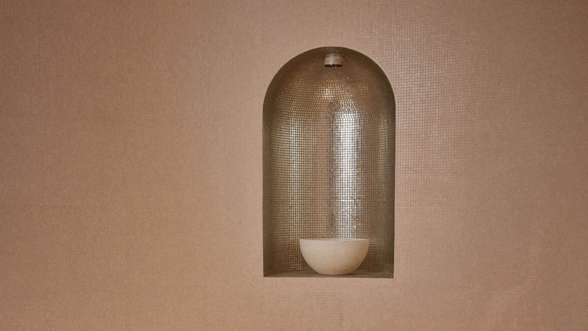 A luxurious steam room with warm-toned walls, a niche featuring a glowing bowl, and a curved seating area designed for comfort.