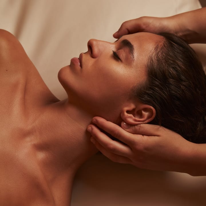 Close-up of a woman receiving a relaxing massage, lying on a treatment bed with soft lighting, skin glowing and expression calm.