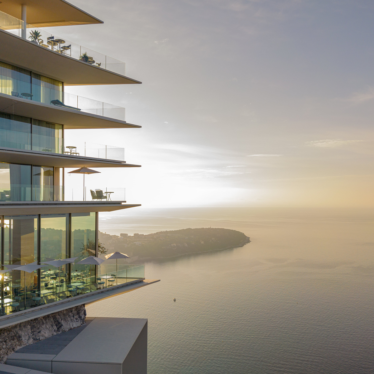 Luxury seafront residence with tiered balconies, glass walls, and sunset reflections over the Mediterranean coastline.