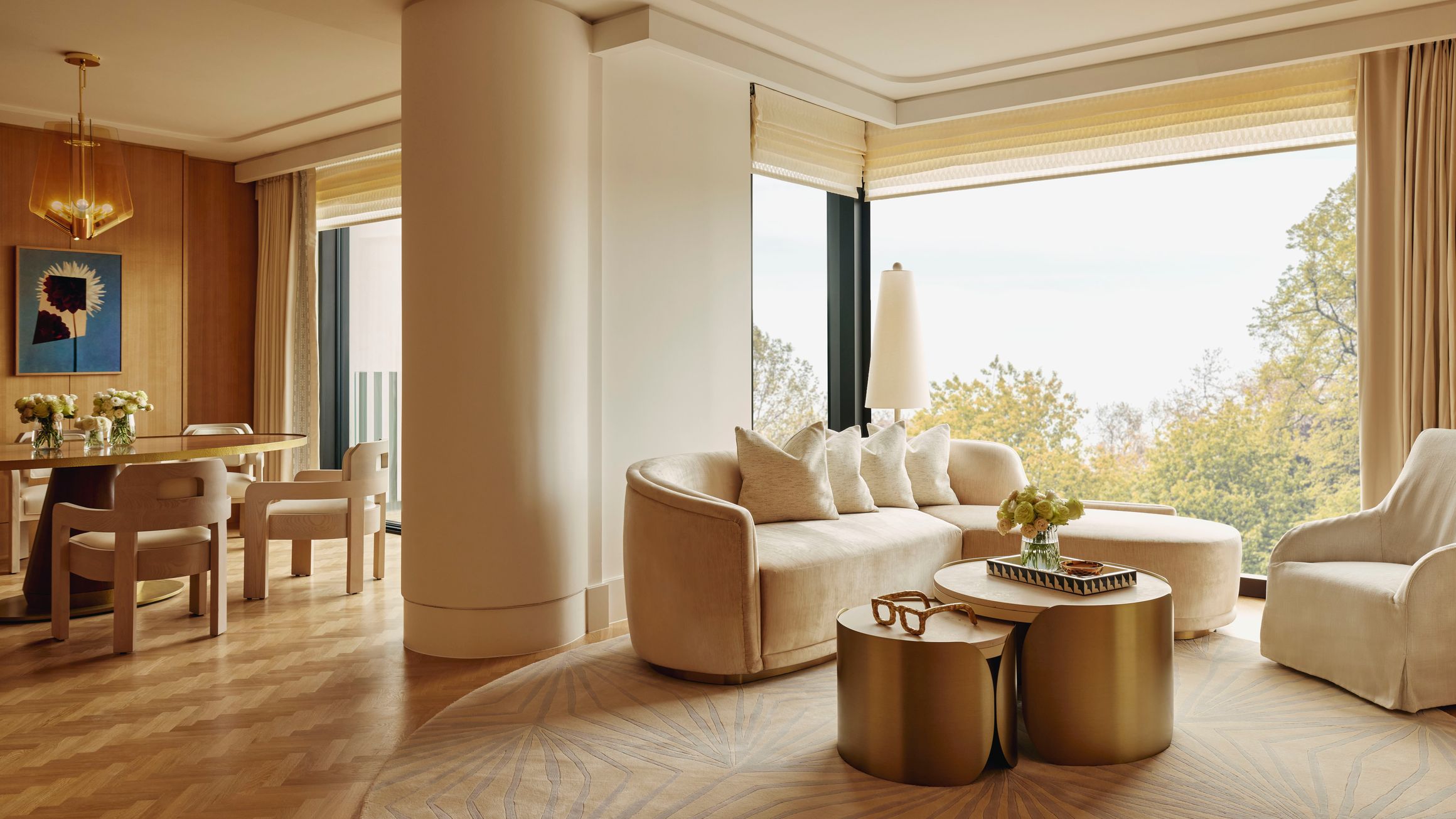 Elegant suite with soft neutral furnishings, gold accent tables, and large windows overlooking treetops.