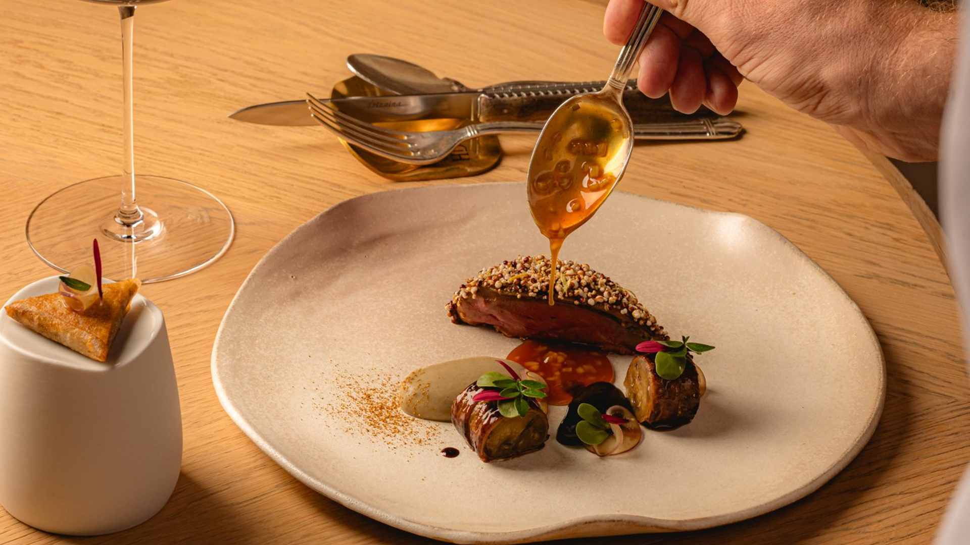 Luxurious plated dish with rich flavors, meticulously finished with sauce, paired with fine red wine in a cozy setting.