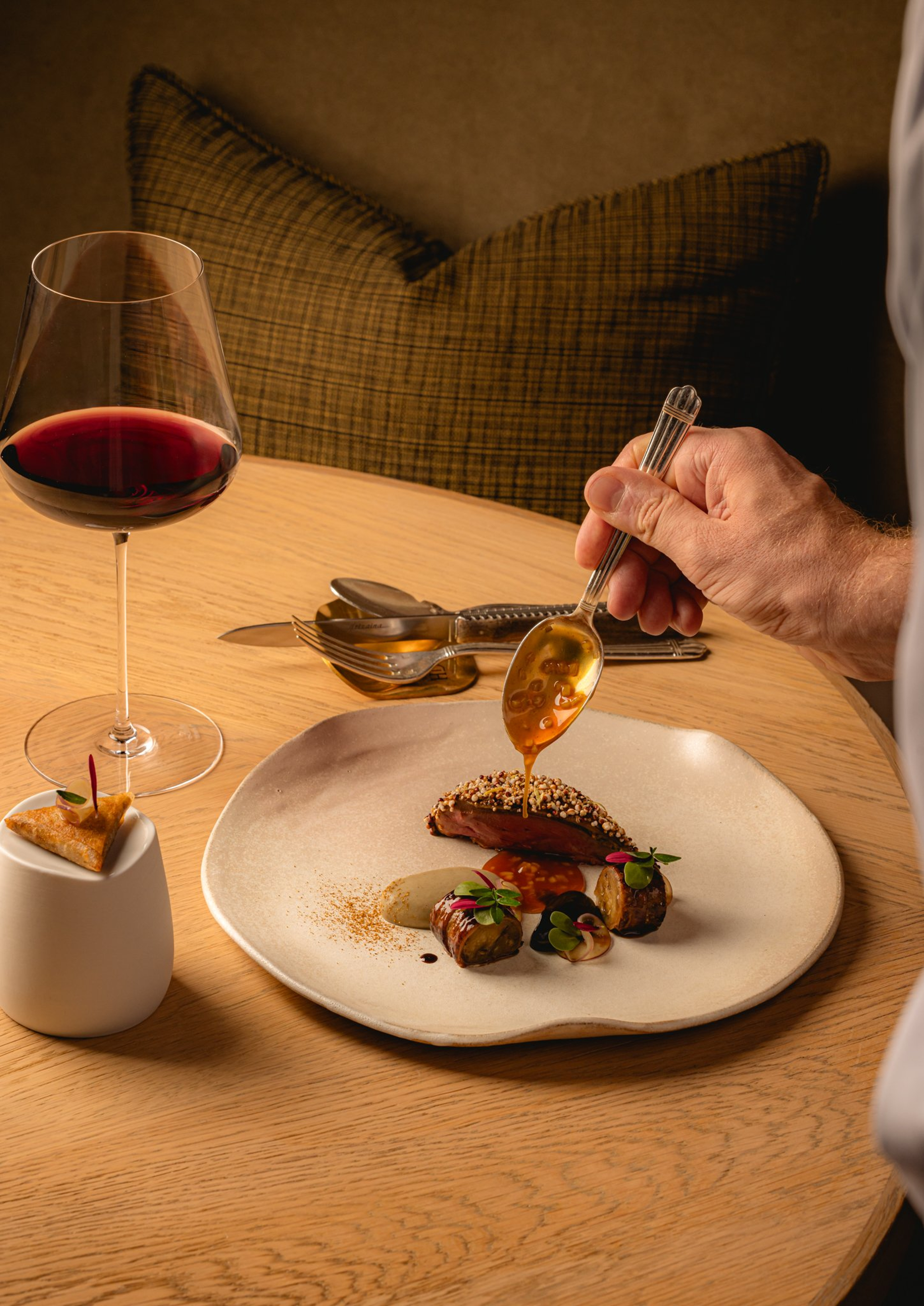 Luxurious plated dish with rich flavors, meticulously finished with sauce, paired with fine red wine in a cozy setting.