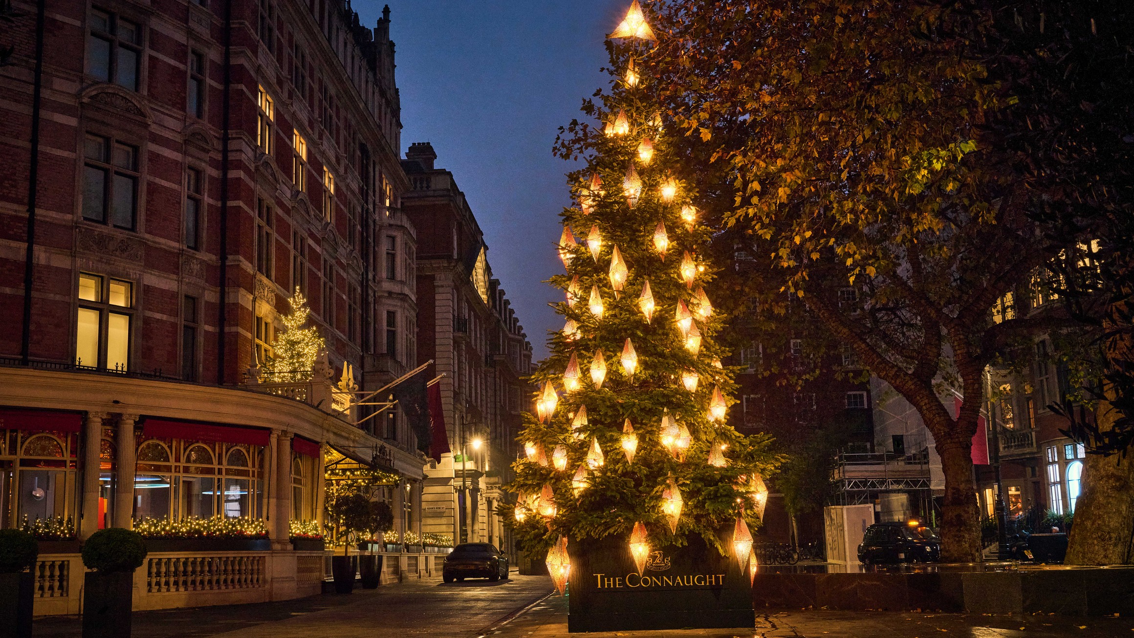 The Connaught’s 2024 Christmas tree glows with golden lanterns in Mount Street’s elegant, festive evening setting.