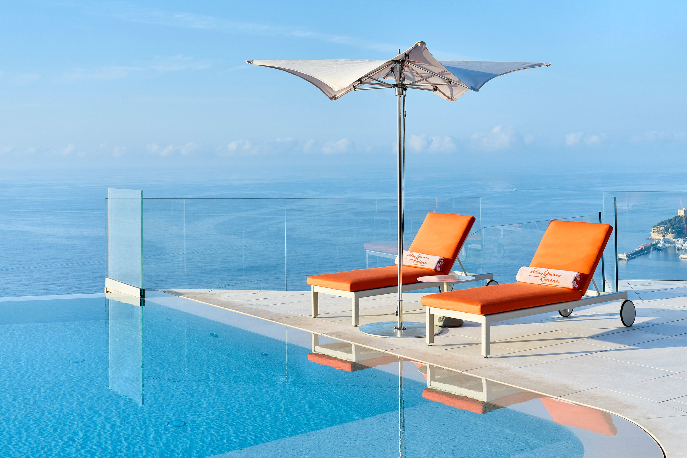 Two vibrant orange sun loungers with an umbrella overlook an infinity pool and the serene ocean horizon.