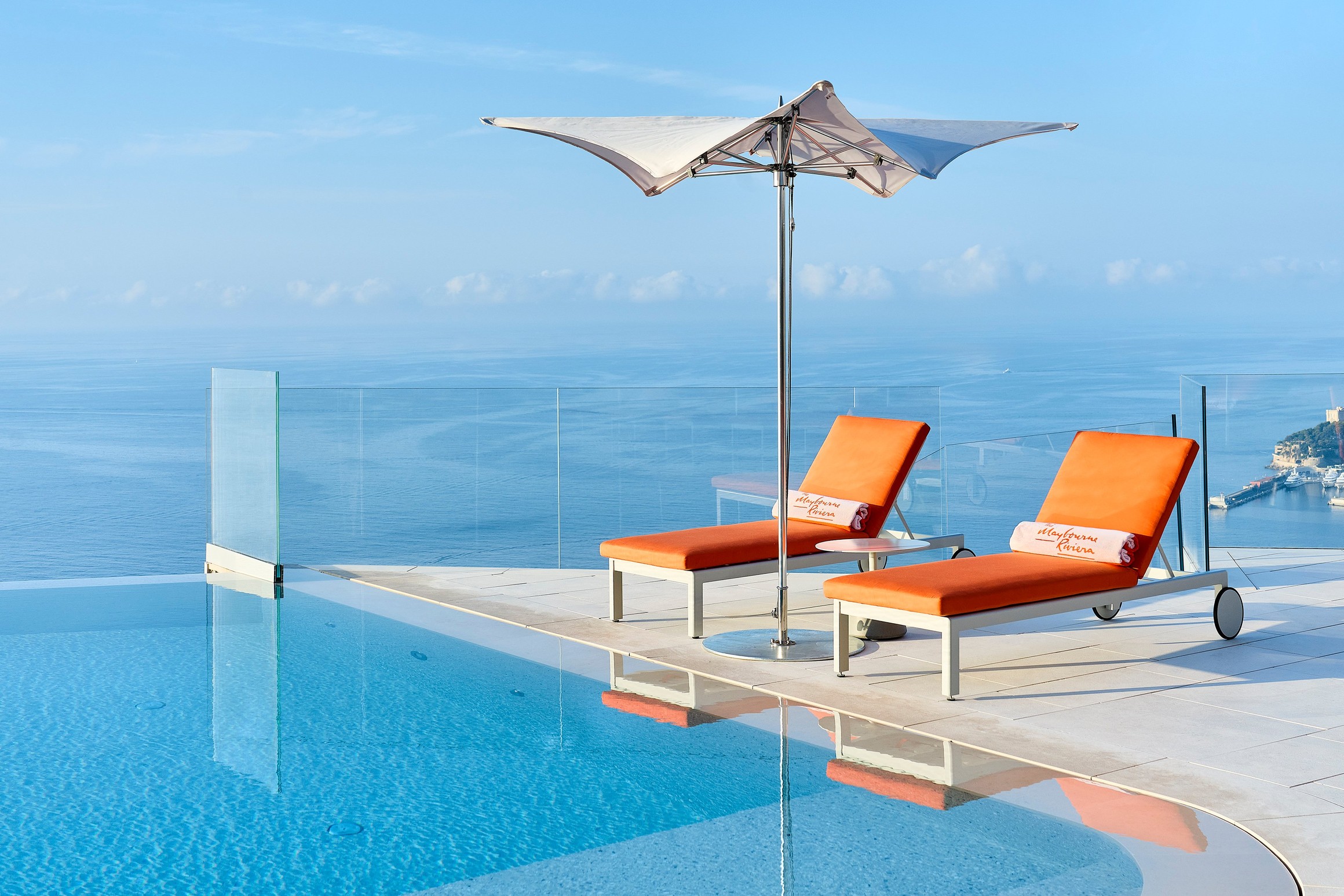 Two vibrant orange sun loungers with an umbrella overlook an infinity pool and the serene ocean horizon.