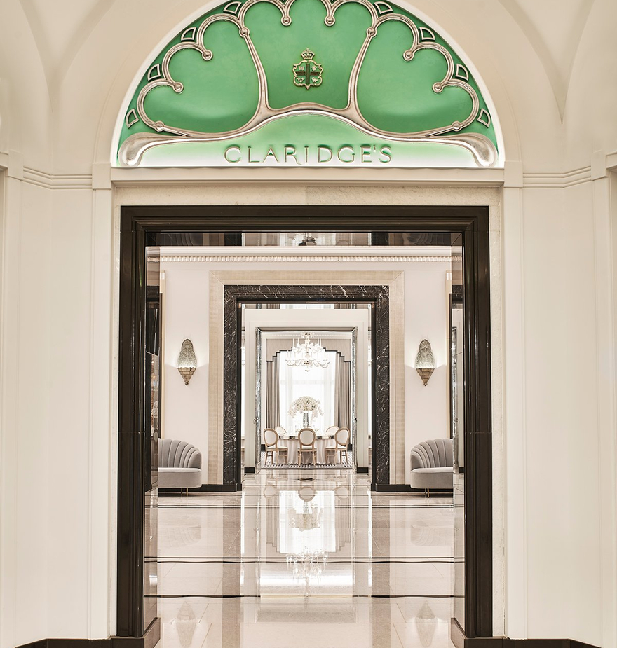 A polished entrance to Claridge's, featuring an ornate green archway, marble flooring, and mirrored hallways.