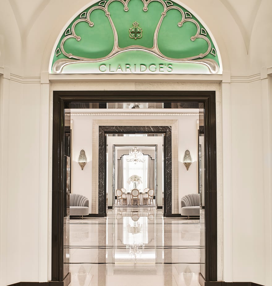 A polished entrance to Claridge's, featuring an ornate green archway, marble flooring, and mirrored hallways.