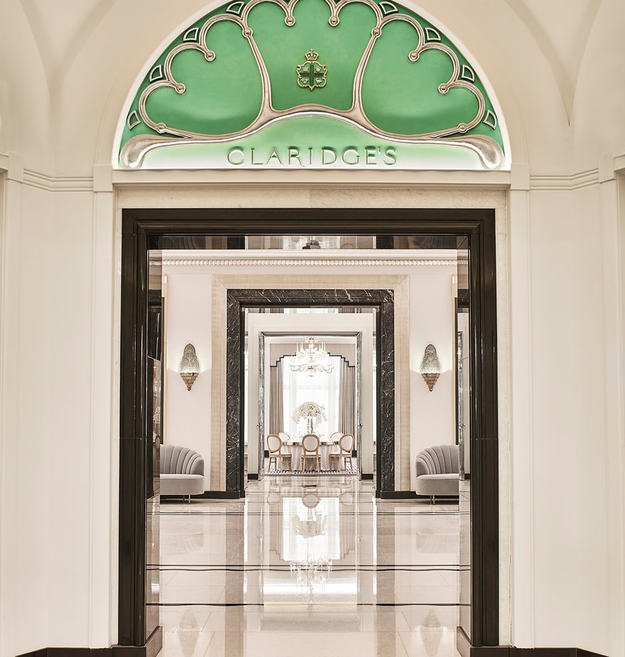 A polished entrance to Claridge's, featuring an ornate green archway, marble flooring, and mirrored hallways.