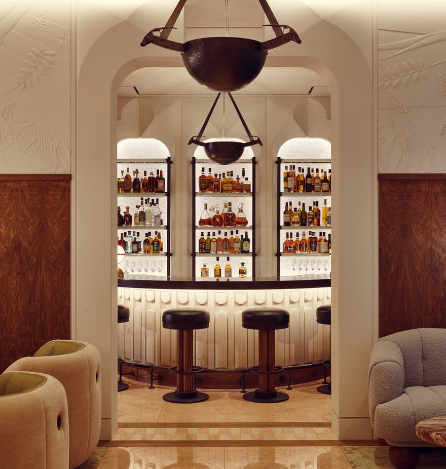 Elegant bar interior with plush seating, warm wood accents, and a backlit display of premium spirits under soft lighting.