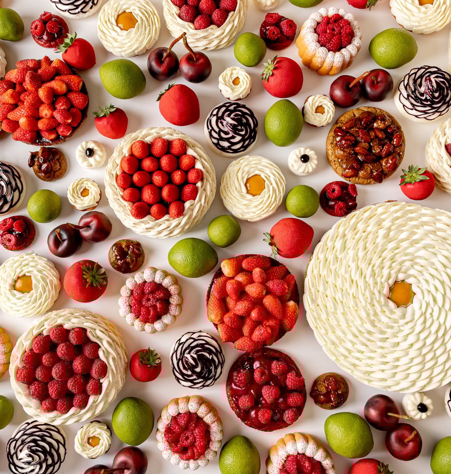 Assorted fruit tarts and fresh fruits arranged on a white surface, including raspberries, strawberries, cherries, figs, and limes.