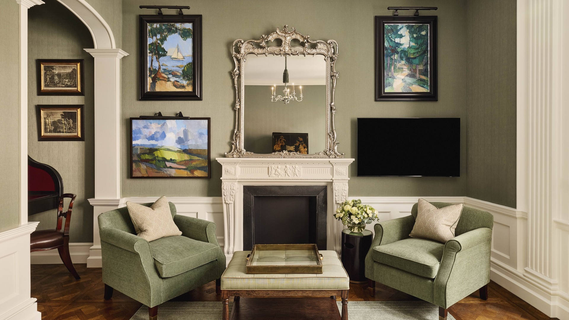 Classic sitting room with green armchairs, a decorative fireplace, and framed artwork on soft green walls.