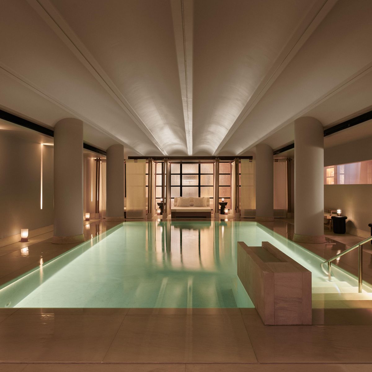 Dimly lit, tranquil indoor pool with soft lighting, cream walls, and loungers, designed for quiet relaxation and accessibility in a luxury spa setting.