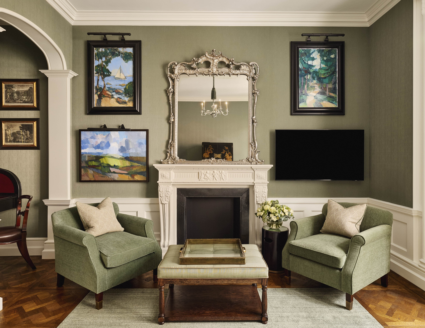Classic sitting room with green armchairs, a decorative fireplace, and framed artwork on soft green walls.