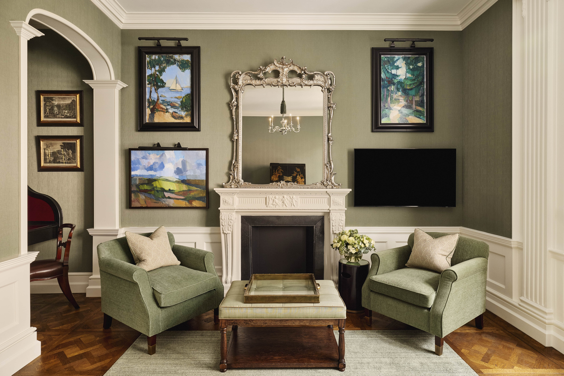 Classic sitting room with green armchairs, a decorative fireplace, and framed artwork on soft green walls.