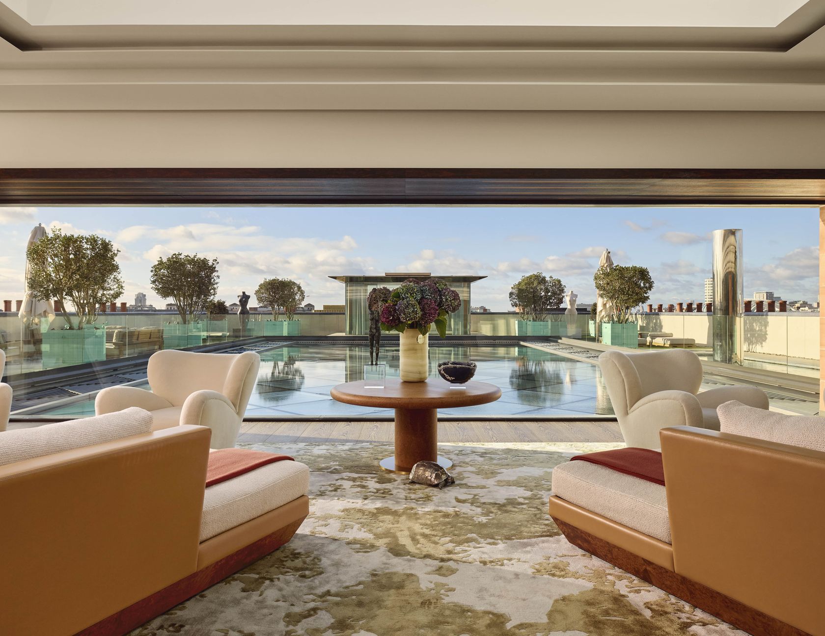 Spacious living area in Claridge’s Penthouse overlooking a private rooftop pool, with plush armchairs and panoramic views across London.