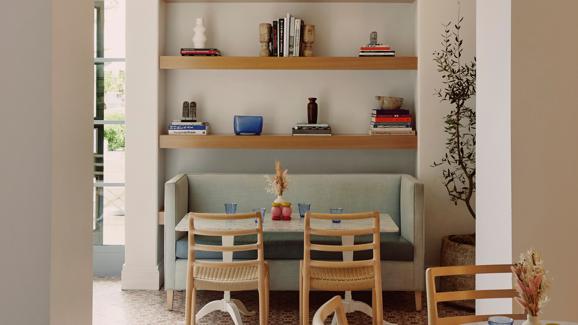 Chic café with patterned tile floors, arched walls, wooden chairs, built-in booth, and minimalist art display.