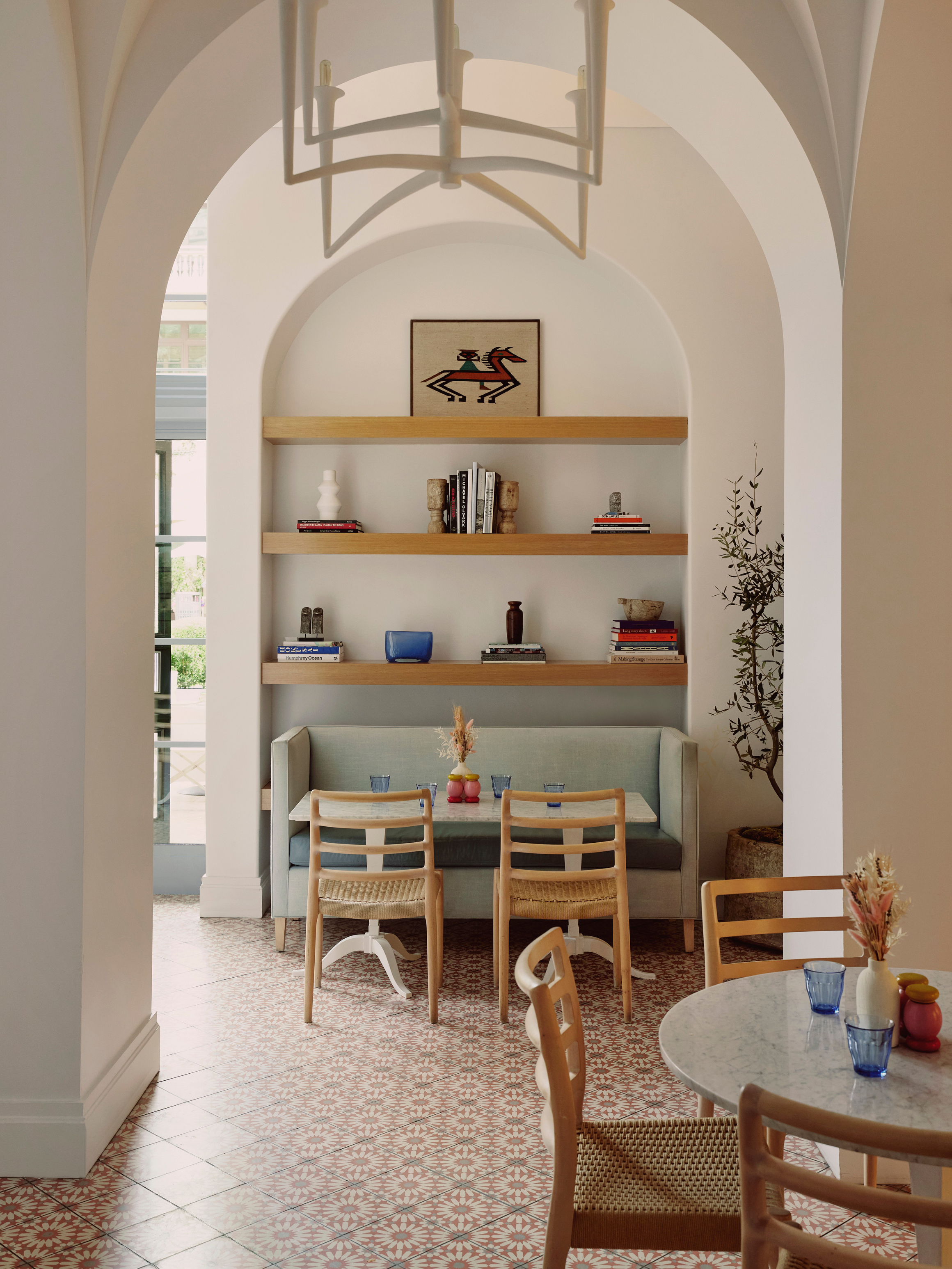 Chic café with patterned tile floors, arched walls, wooden chairs, built-in booth, and minimalist art display.