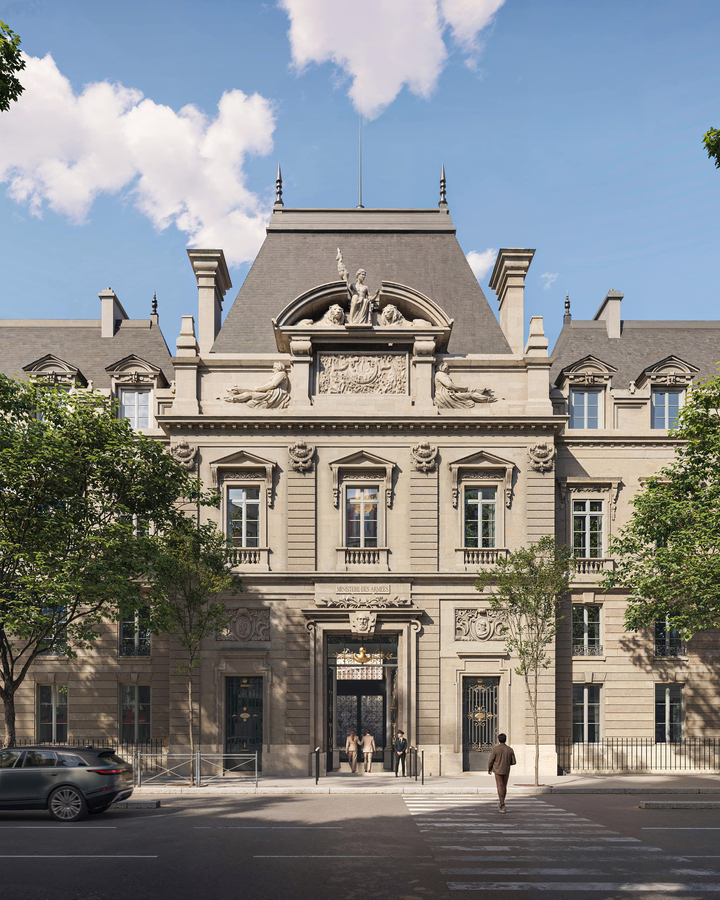 Grand Parisian hotel entrance with ornate stone façade, mansard roof, and classical sculptures, framed by trees and city street.