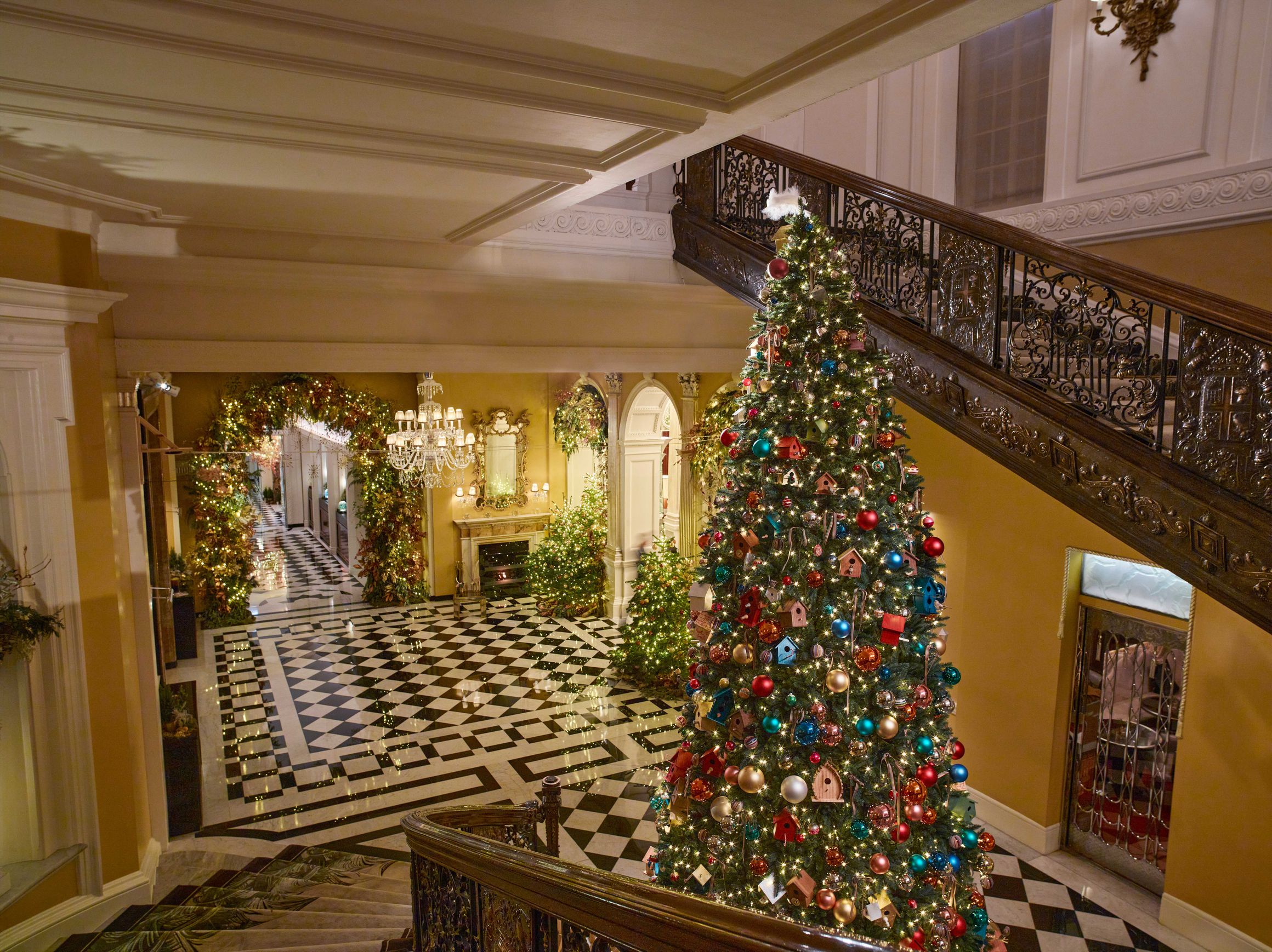 Claridge’s lobby with grand staircase and 2024 Christmas tree adorned with birdhouses, baubles and warm white lights.