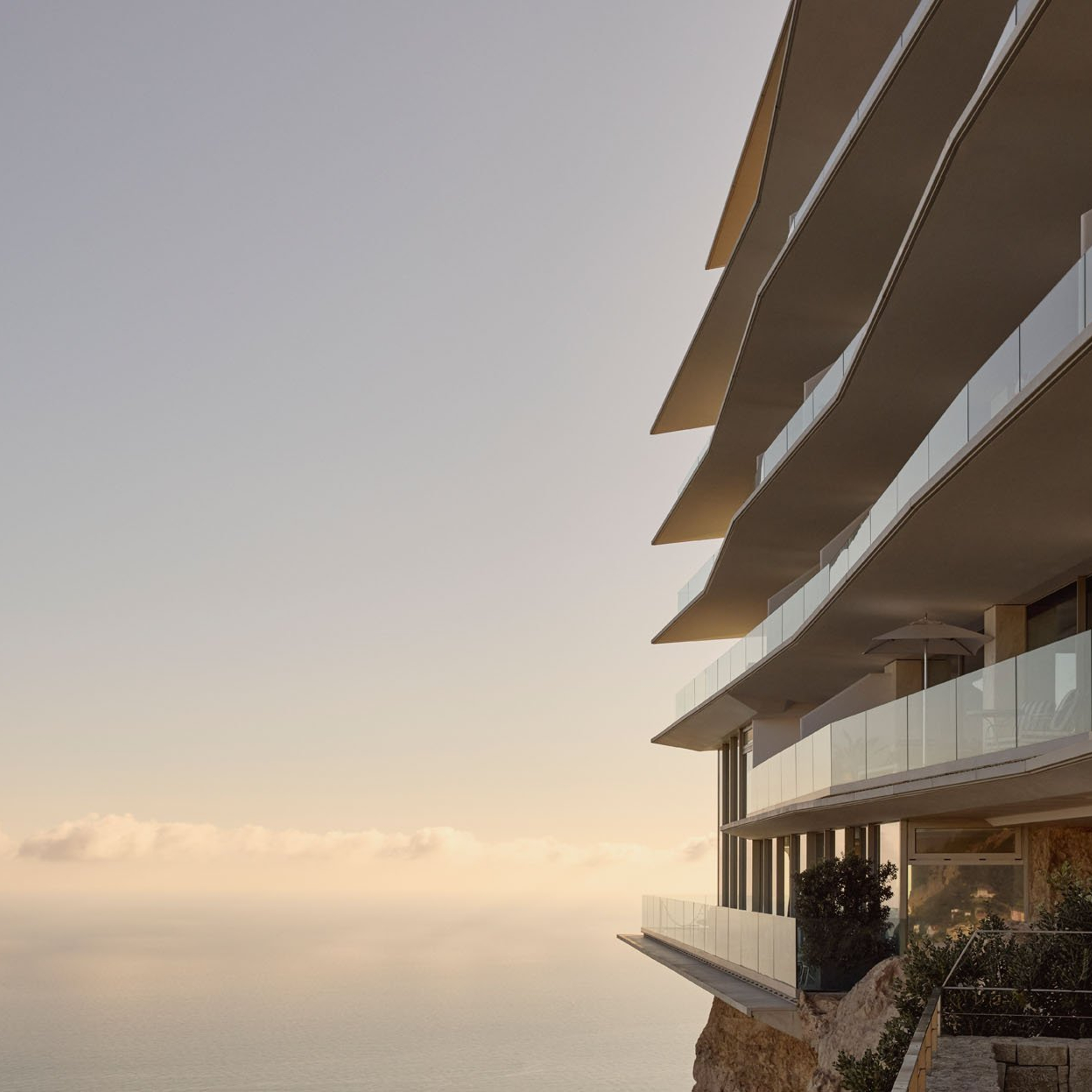 Modern cliffside hotel with cascading glass balconies overlooking a calm, sunlit sea, set against a pastel sky at golden hour.