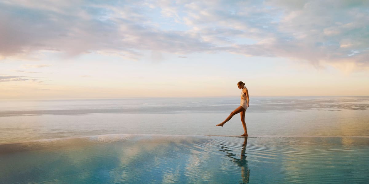 Woman walking on the edge of an infinity pool with the sky behind her