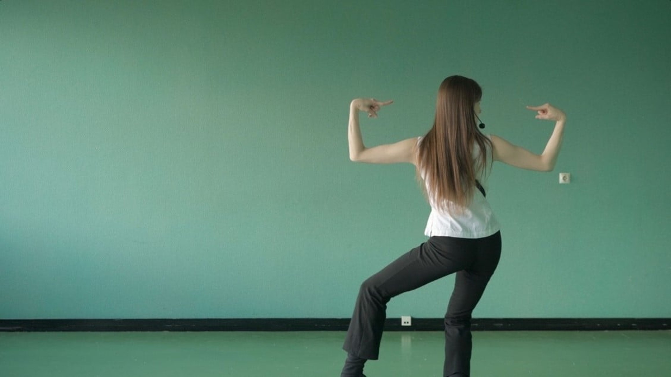 Woman striking a dynamic dance pose against a teal wall, showcasing strength and balance.