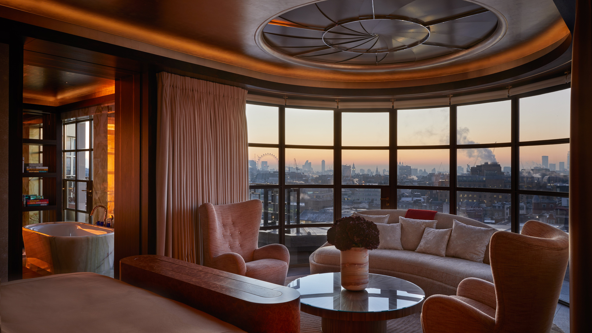 An elegant lounge illuminated by a geometric skylight, showcasing curated decor, a marble fireplace, and expansive city views framed by floor-to-ceiling windows