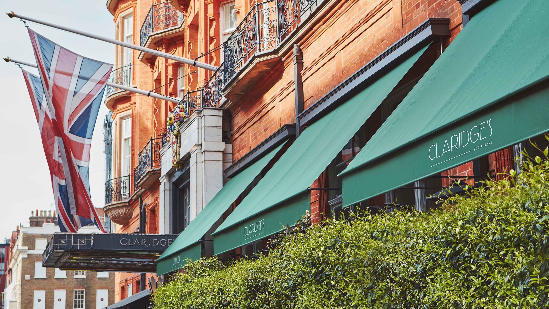 The iconic red-brick façade of Claridge’s, adorned with green awnings and a Union Jack, epitomizing timeless British elegance.